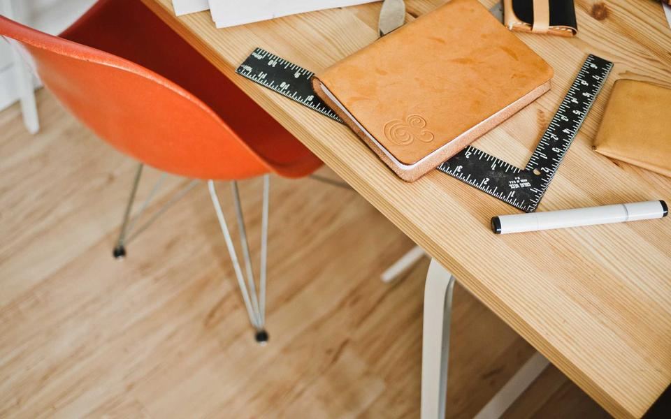 Sedia arancione a una scrivania in legno chiaro con quaderno, righello e penna
